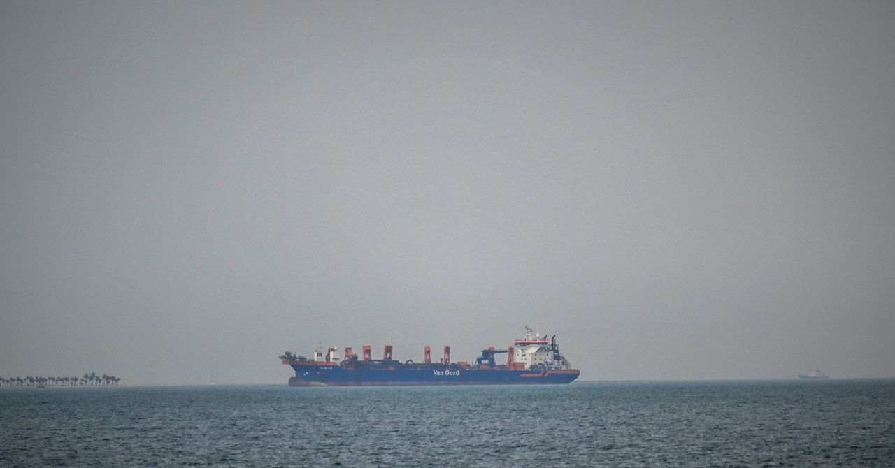 Rusting ship stranded in Strait of Hormuz with crew on deck amid tense Gulf waters