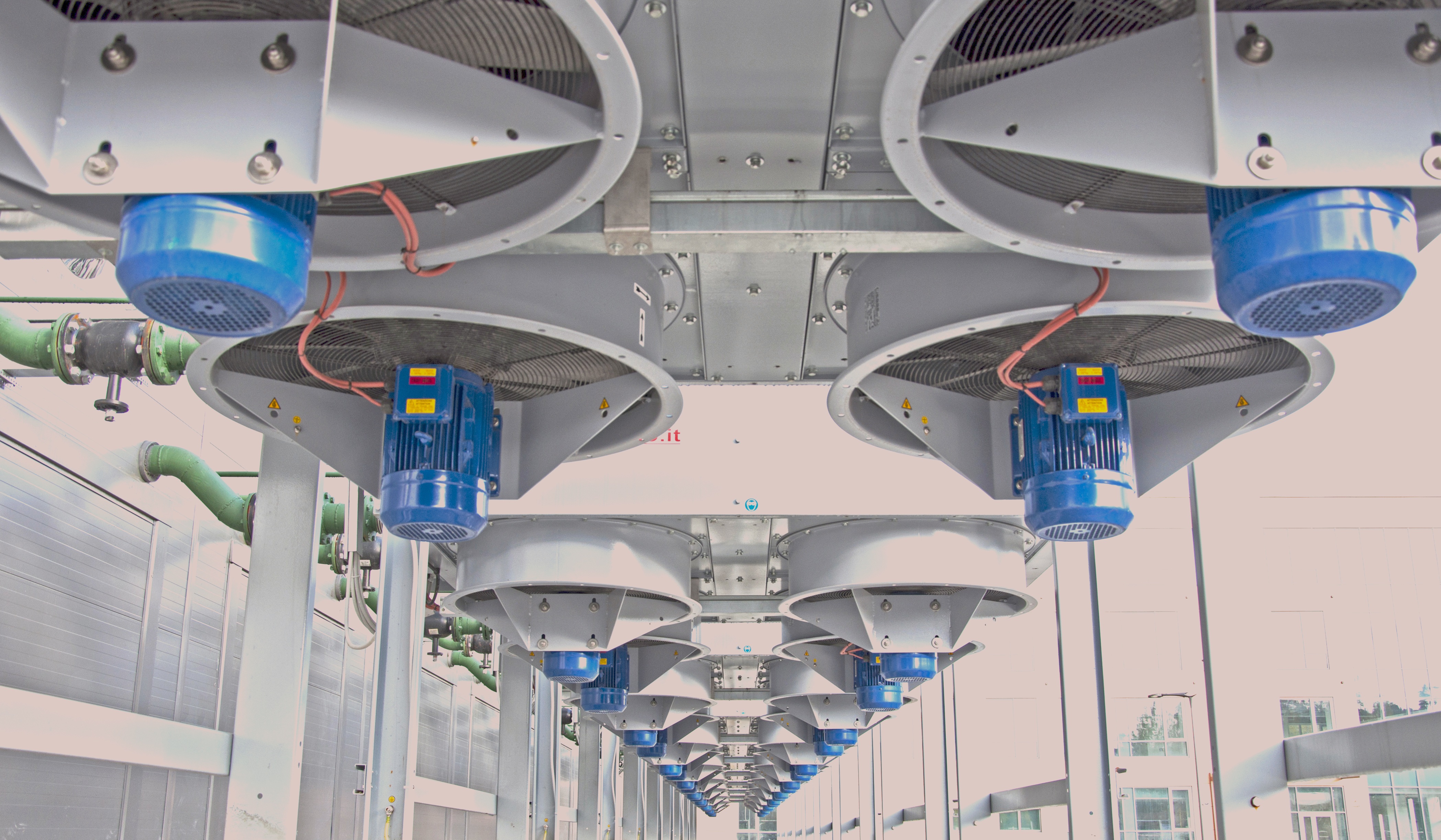 Aerial view of a massive AI data center with visible heat exhaust plumes rising into a hazy urban skyline at dusk