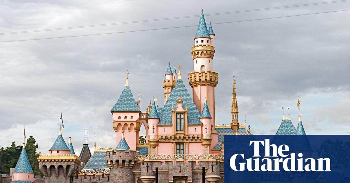 A person walking through a Disneyland entrance gate with a camera visible overhead, suggesting surveillance.